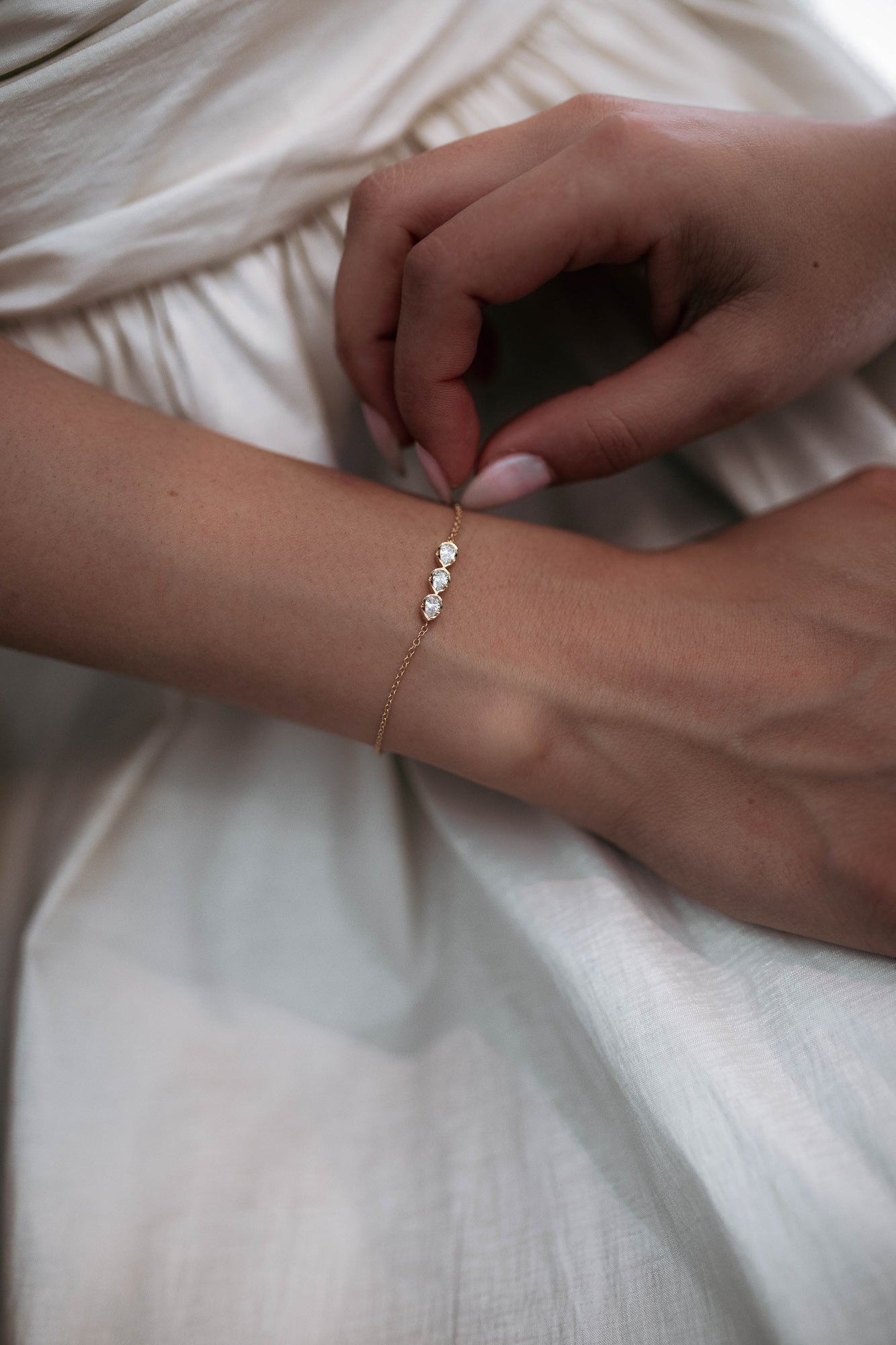 Close-up of hands fastening the Sereine bracelet, crafted from 18k yellow gold and adorned with pear-shaped diamonds totaling approximately 0.4 ct. This timeless and elegant piece is available with natural or lab-grown diamonds.