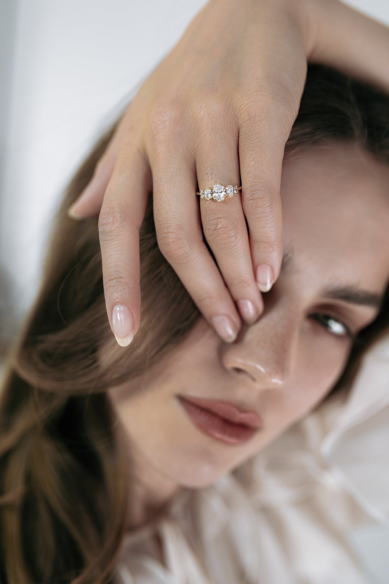 Close-up of a model wearing the La Blossom engagement ring by Presiada, crafted in 18K gold. Featuring a central diamond surrounded by five oval diamonds in a unique and delicate arrangement, this one-of-a-kind ring exudes timeless beauty and sophistication. Available in yellow or white gold, customizable with natural or lab-grown diamonds.