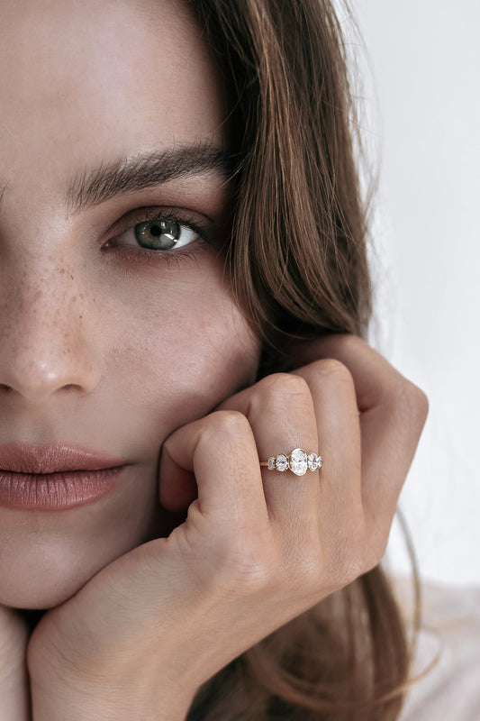 Close-up of a model wearing the La Blossom engagement ring by Presiada, crafted in 18K gold. Featuring a central diamond surrounded by five oval diamonds in a unique and delicate arrangement, this one-of-a-kind ring exudes timeless beauty and sophistication. Available in yellow or white gold, customizable with natural or lab-grown diamonds.