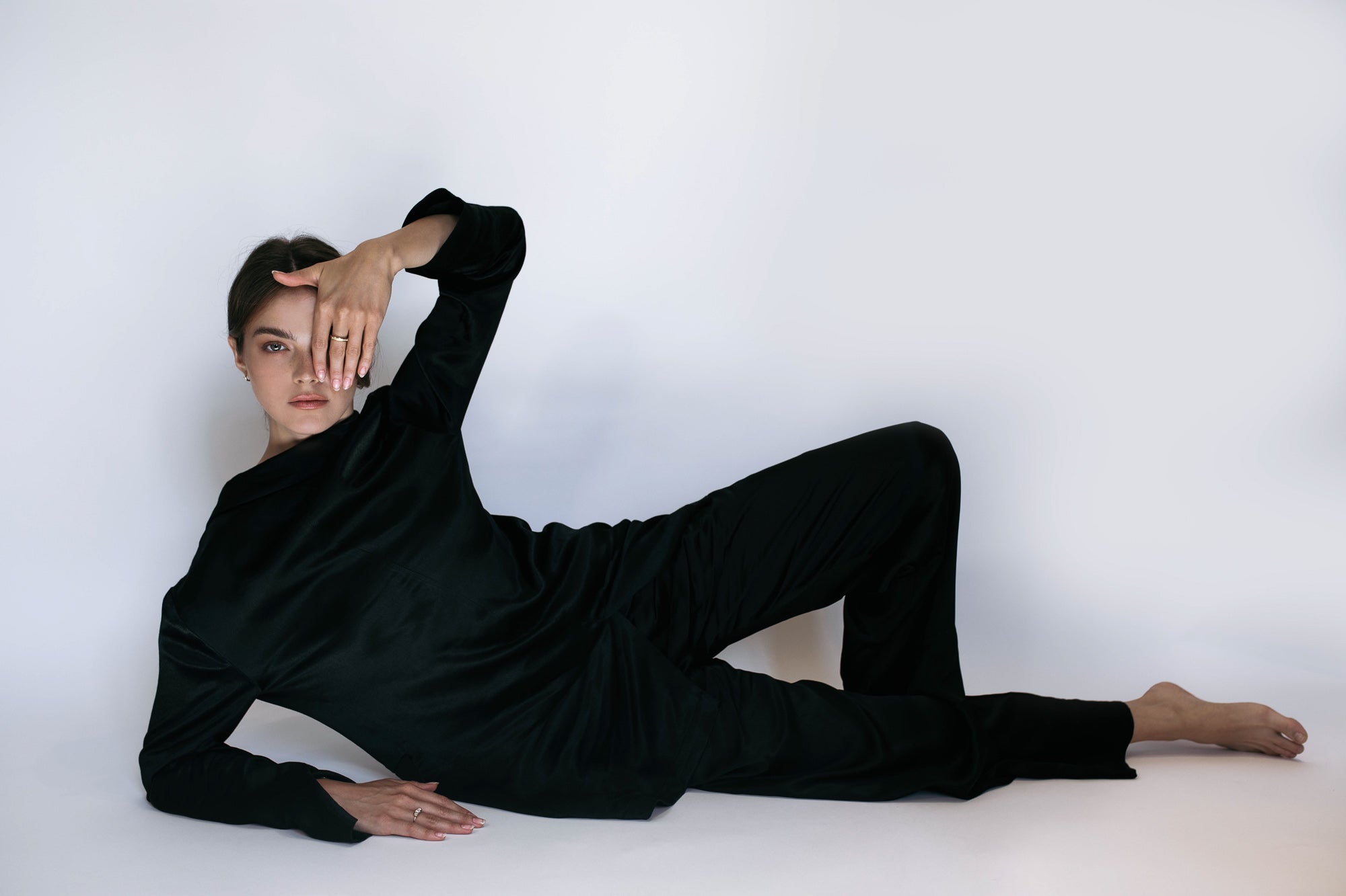 Artistic shot of a model dressed in a sleek black outfit, striking a relaxed pose while wearing the L’Arc ring by Presiada. Although the ring is not the focal point, the composition highlights elegance and contemporary style. The L’Arc ring is crafted in 18K gold with pavé-set diamonds, available in natural or lab-grown options.