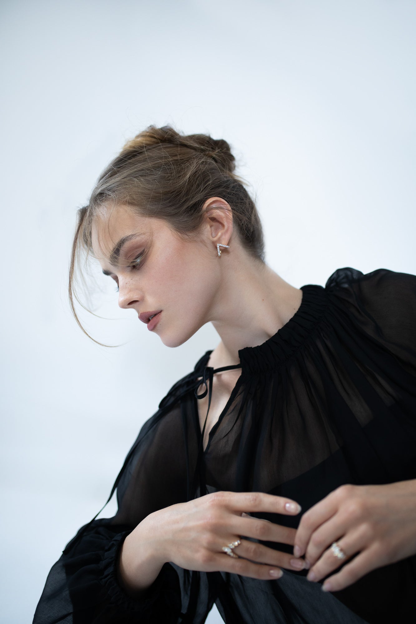 Model wearing the Vivid Earrings by Presiada, featuring a unique V-shaped design that sits elegantly at an angle on the ears. These earrings are crafted in 18K gold and set with 0.75 carats of diamonds, available in both natural and lab-grown options. A bold statement piece showcasing modern design and impeccable craftsmanship. The J’ador V-Flame and La Divine rings, also worn by the model, are out of focus in the image.